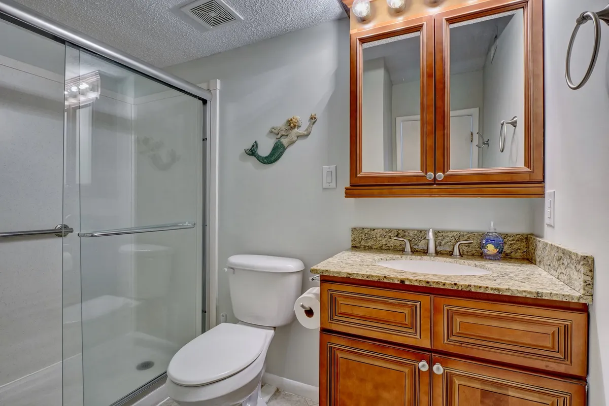 A bright bathroom featuring a granite countertop, glass shower stall, wooden cabinetry, and playful mermaid decoration. The environment is both practical and welcoming, ideal for showcasing areas where guests might use their own towels or linens.