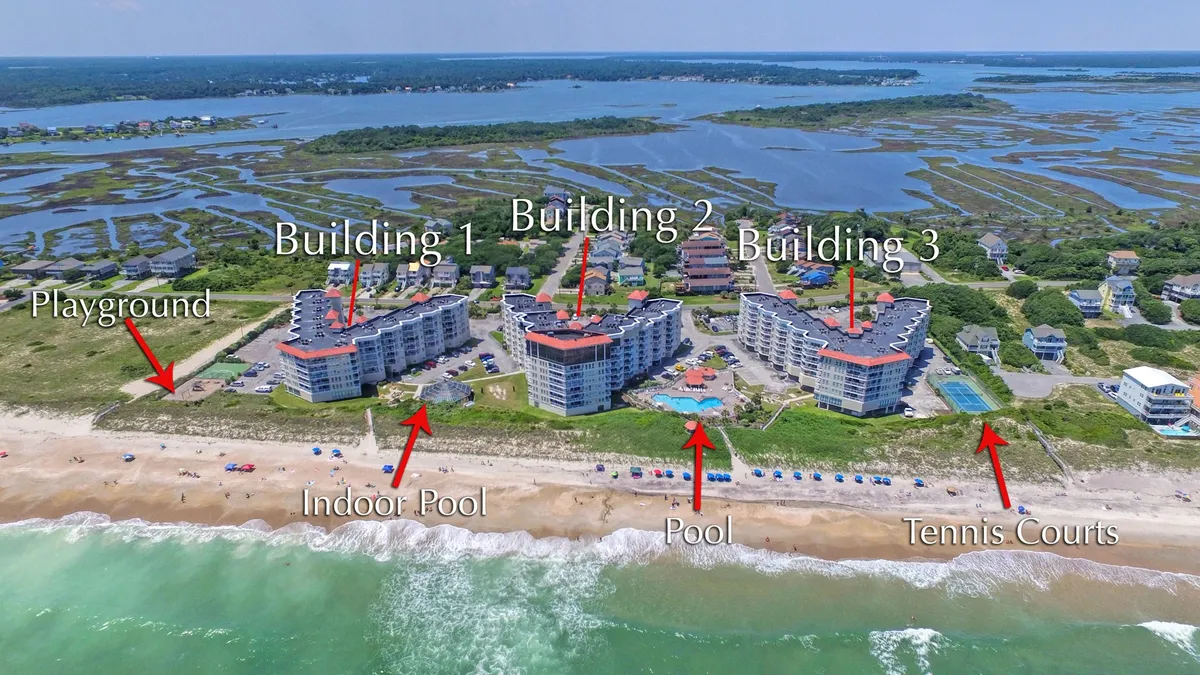 A wide exterior shot showcasing the St. Regis resort grounds, including multiple pools, a playground area, tennis courts, and glimpses of the ocean and beach beyond. Families can be seen swimming, playing, and engaging in various activities across the property.