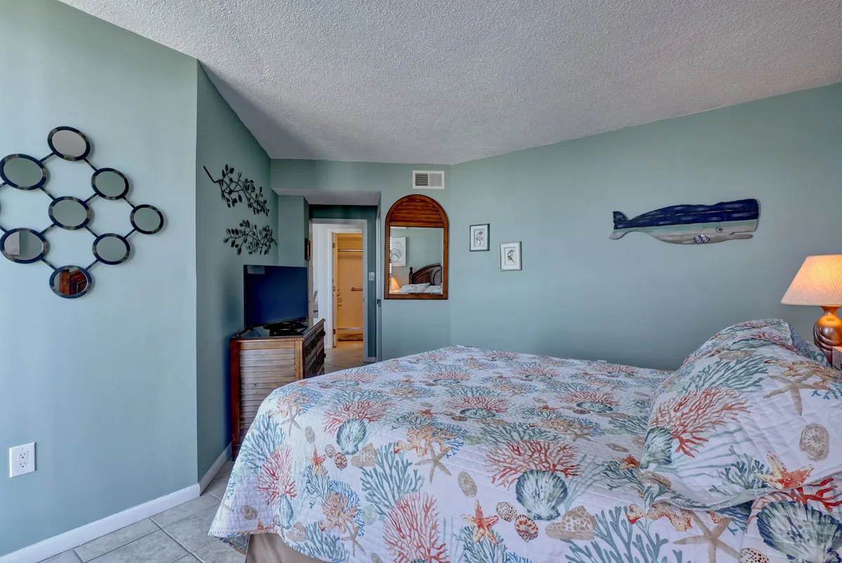 A serene bedroom with a bed dressed in coral-patterned bedding, whimsical whale wall art, and mirrored decor. The space feels inviting and fresh, perfect for personalizing with your own linens or enjoying a premium linen package.