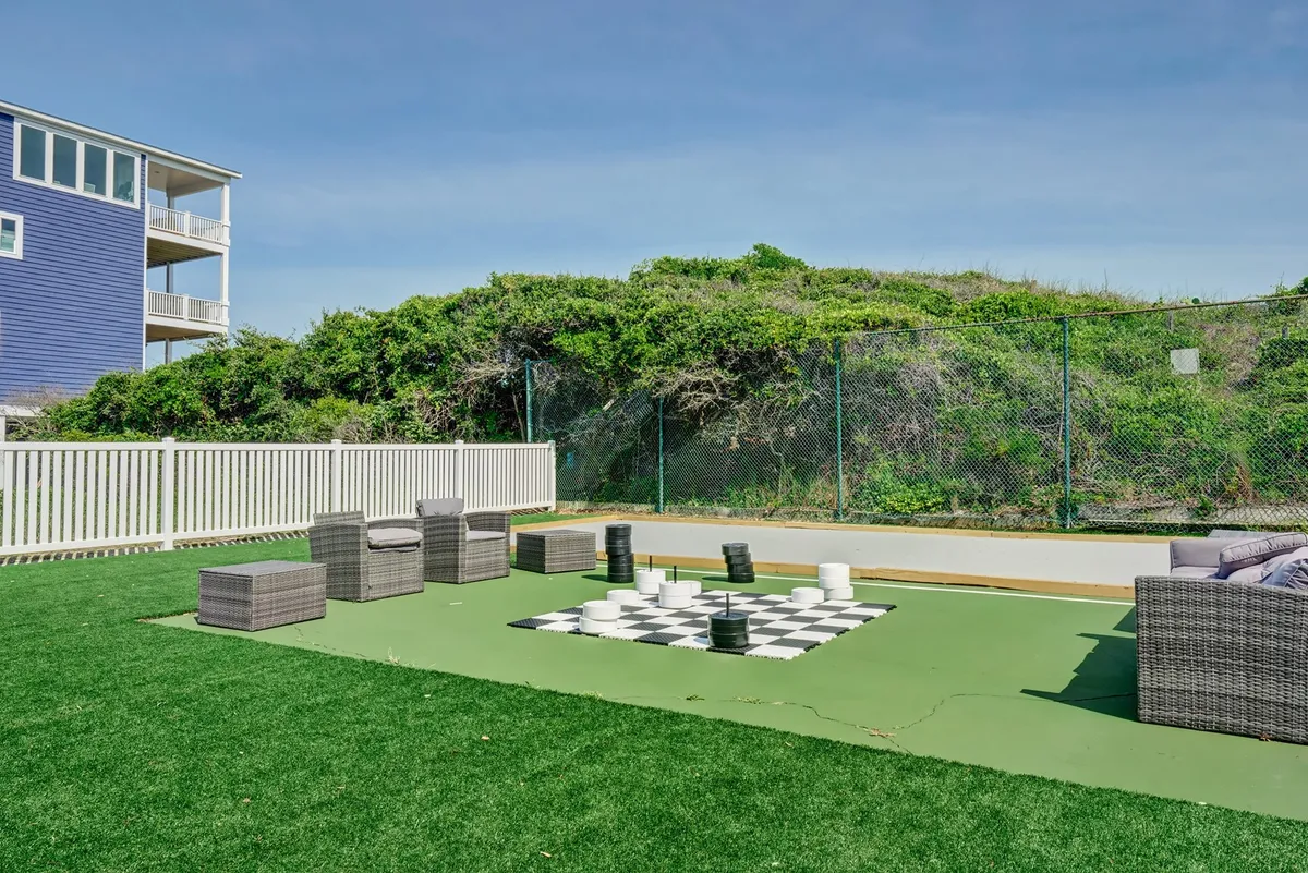 This exterior image highlights a large chessboard set on a green lawn, bordered by modern seating areas. The space invites guests to enjoy playful afternoons or sunset gatherings in a lively, social atmosphere.