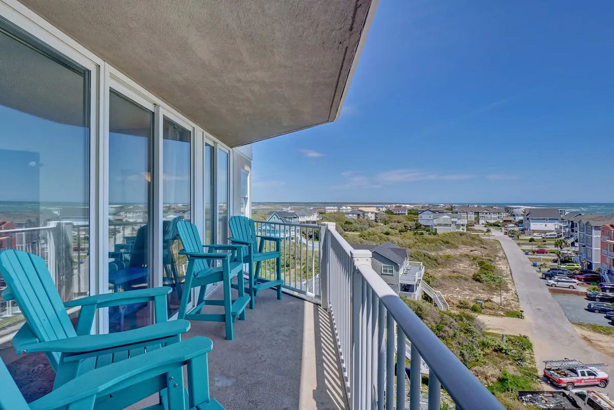 A serene balcony scene with blue Adirondack chairs overlooking a panoramic ocean vista. The balcony railing frames endless water views, inviting guests to relax, sip coffee, or watch the sunrise and sunset, seamlessly blending indoor comfort with nature.